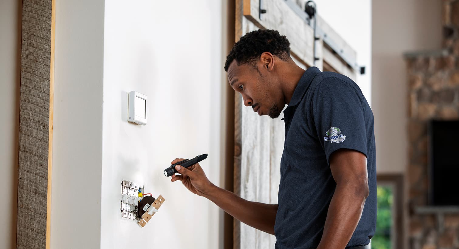 A professional Sansone electrician using a flashlight to safely inspect and troubleshoot exposed residential wall switch wiring during an electrical repair service.