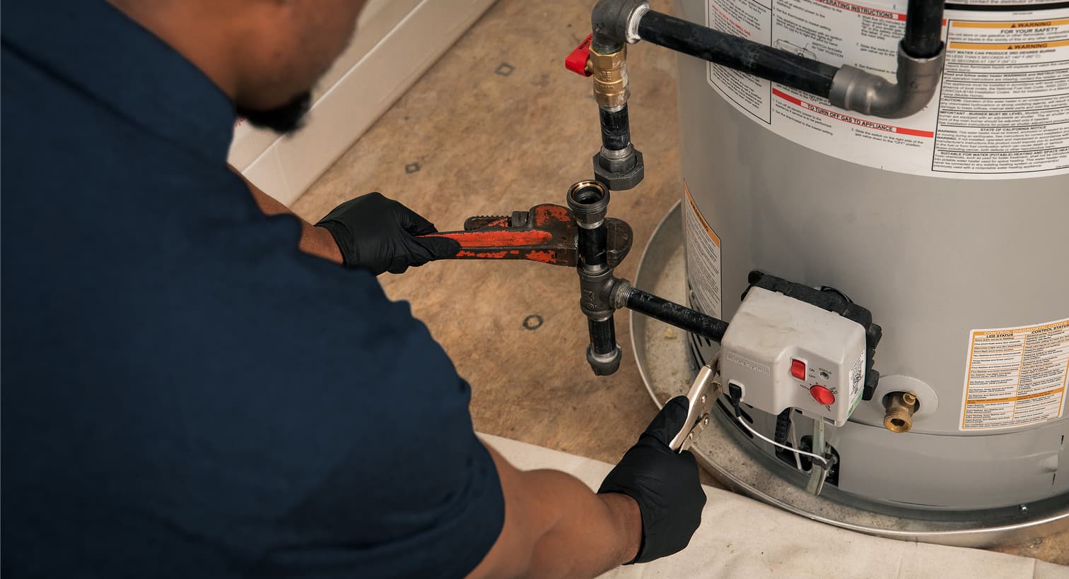 A professional Sansone plumber using a pipe wrench to fix a residential water heater during a home plumbing repair service.
