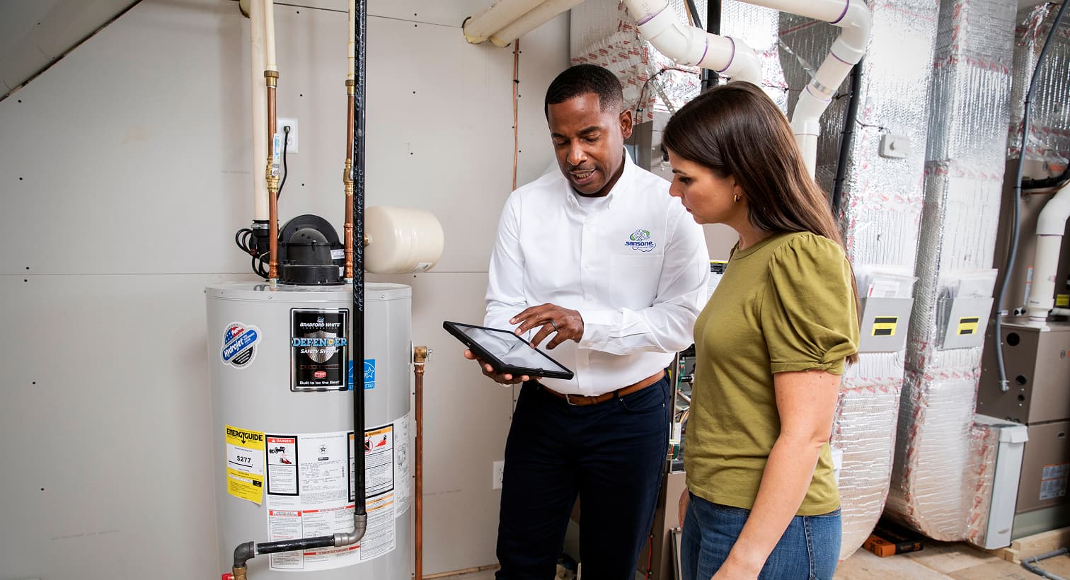 A Sansone plumber using a tablet to discuss residential water heater services, repairs, and replacement options with a homeowner.
