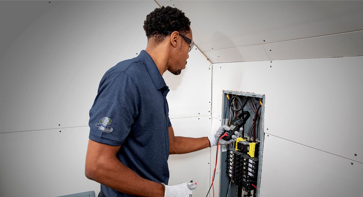 A professional Sansone electrician using a digital multimeter tool to test and inspect a residential electrical panel during a circuit breaker service call.