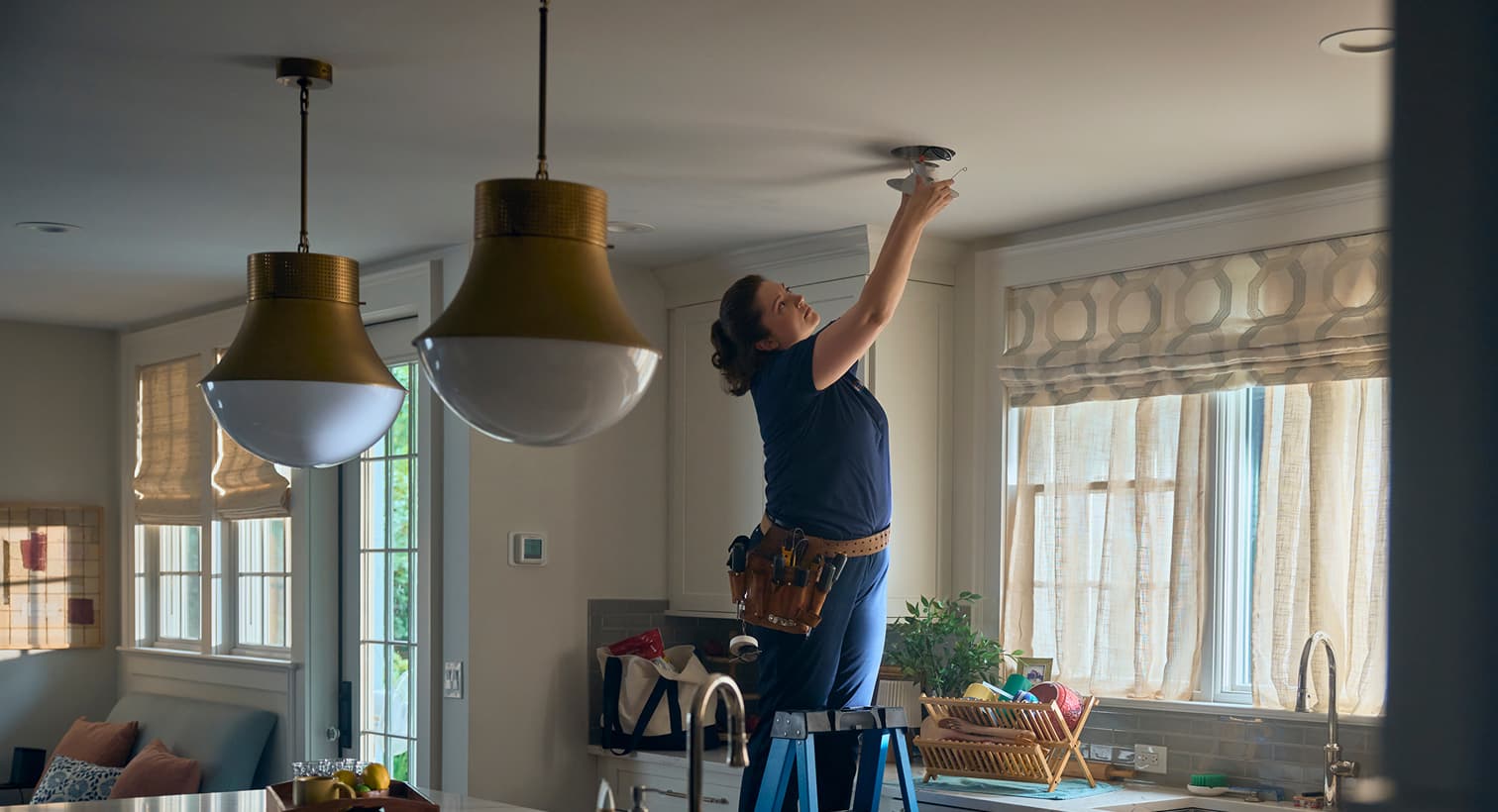 A professional Sansone electrician standing on a ladder to install modern recessed ceiling lights during a residential electrical installation service.